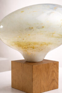 Sculptural hand-blown glass lamp with organic form and subtle green-gold texture, presented in a refined gallery-style interior.